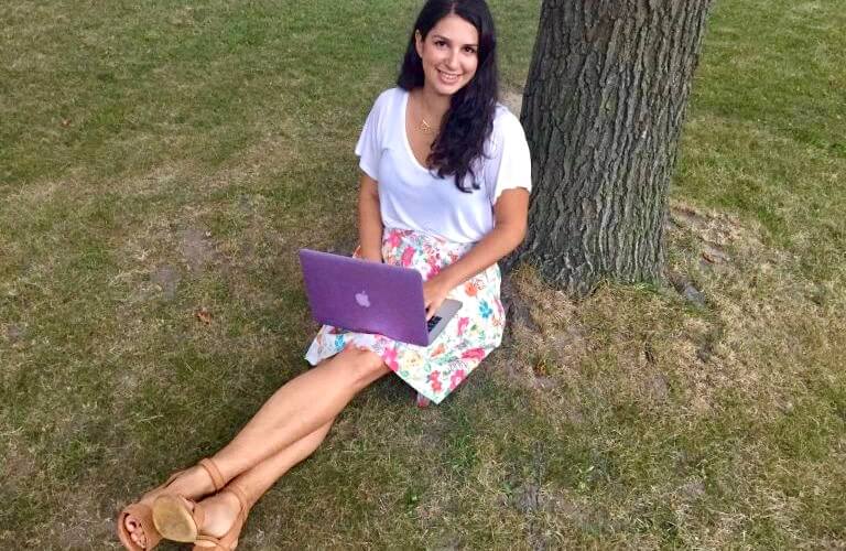 Kayla Kurin works on her laptop while sitting under a tree