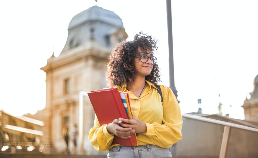 A young woman smiles as she carries school books