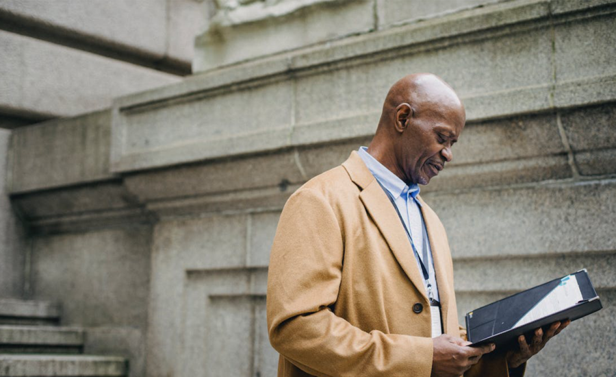 An employee in a beige suit stands outside looking at his pension plan summary in a folder.