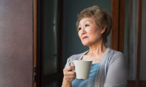 A middle-aged woman, holding a mug, gazes out the window