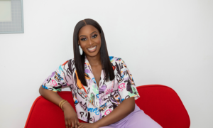 Canadian financial influencer Reni Odetoyinbo smiles at the camera while sitting on a red armchair.
