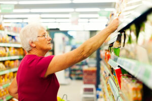 A senior-aged woman reaches for a product on a supermarket shelf