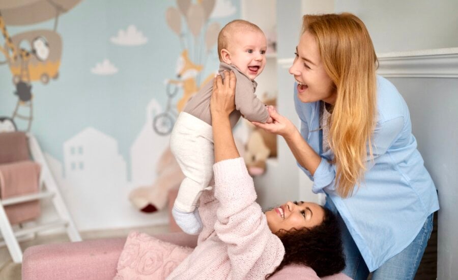 Two moms play with a baby in a nursery