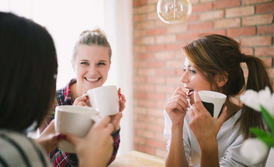 Three diverse young women chat and drink coffee