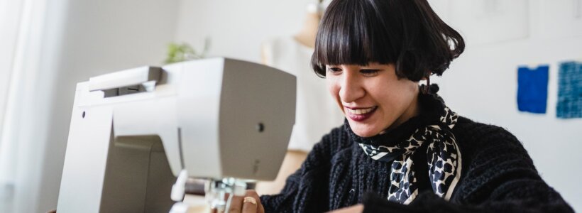 A smiling young woman works on a sewing machine