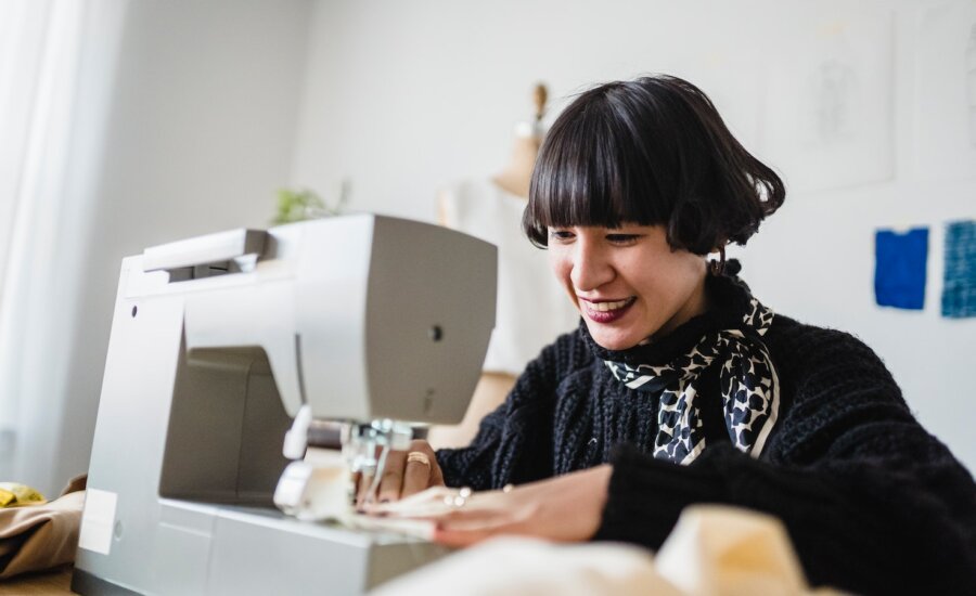 A smiling young woman works on a sewing machine