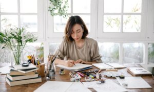 A woman with a side hustle works diligently on her artwork at her desk.