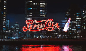 A giant red light-up Pepsi Cola sign at night time.