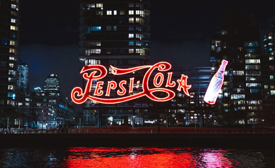 A giant red light-up Pepsi Cola sign at night time.
