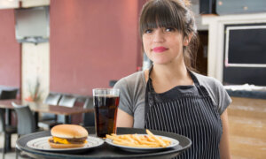 A young woman holds a tray with burger, fries and soda