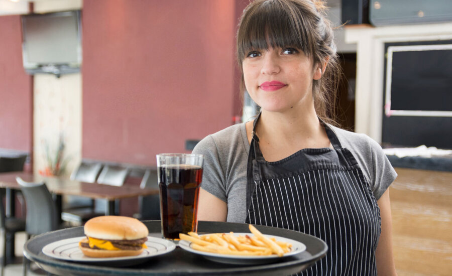 A young woman holds a tray with burger, fries and soda