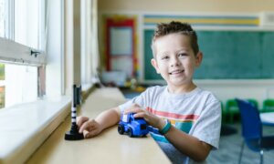 A young boy plays with a toy car in a classroom