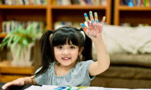 A young girl raises her hand while fingerpainting