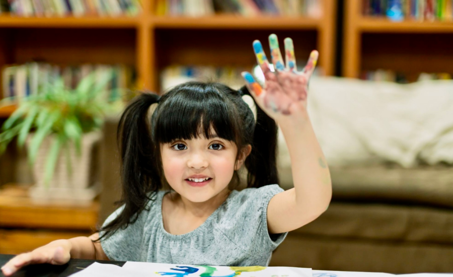 A young girl raises her hand while fingerpainting