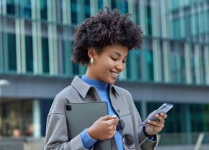 A smiling young woman looks at her phone on a downtown street.