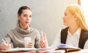 Two woman discuss the tax implications of a company acquisition over coffee