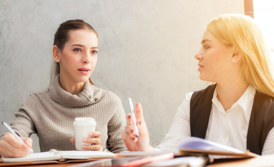 Two woman discuss the tax implications of a company acquisition over coffee