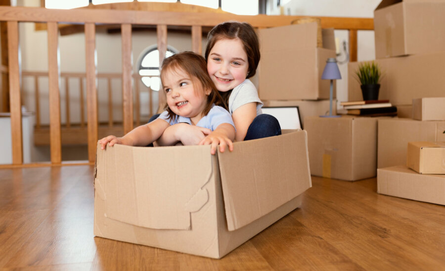 Two young sisters hugging in a cardboard box after moving into a new home