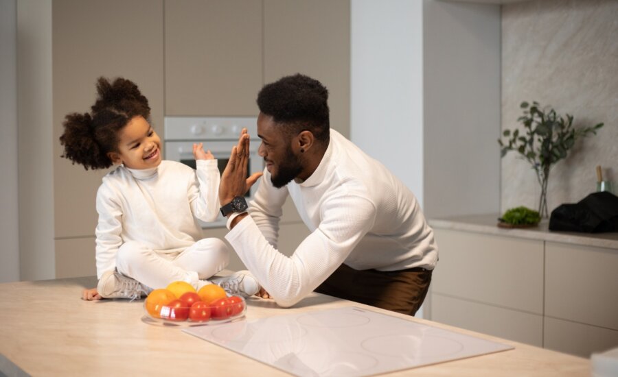 A father high-fives his daughter in the kitchen