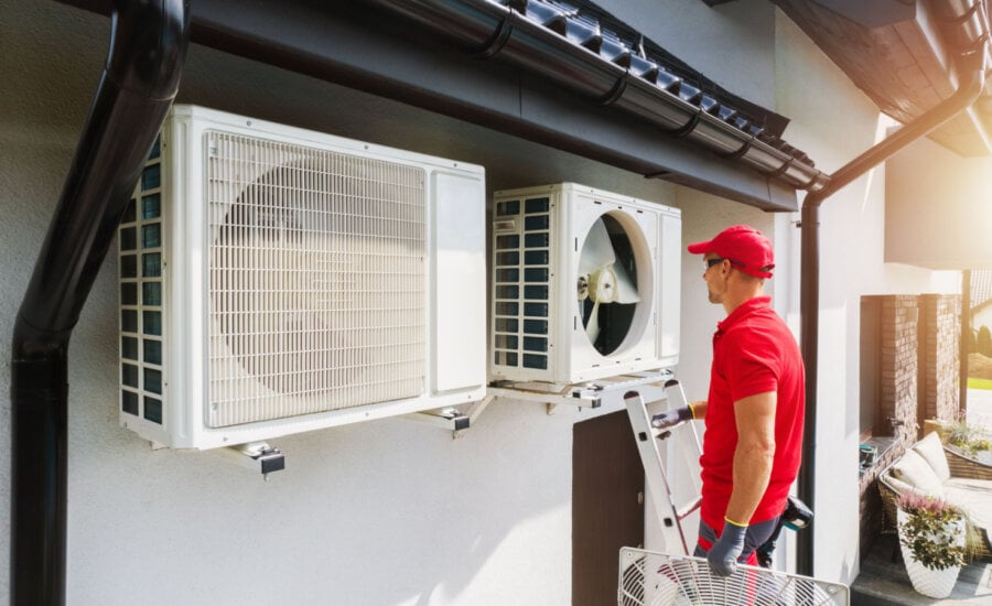 A technician works on a heat pump attached to a house