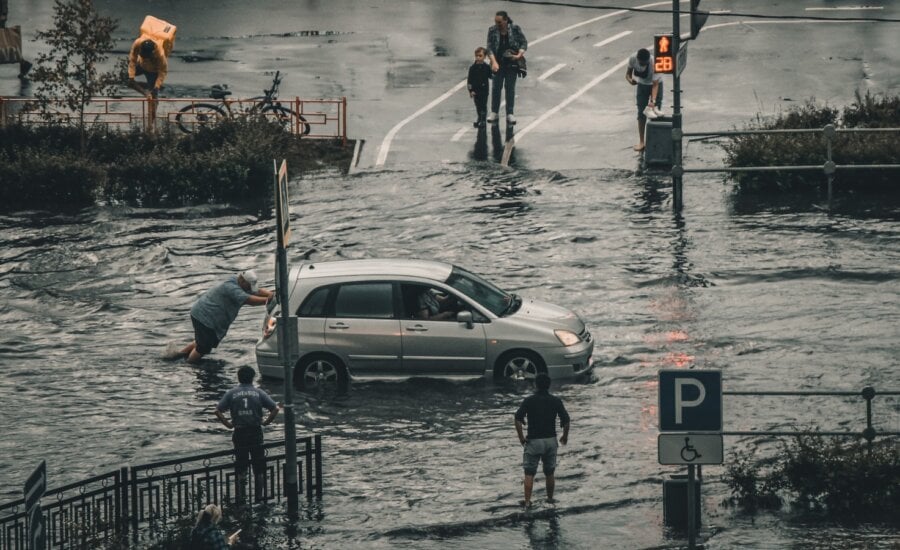 A man pushes his vehicle along a flooded road