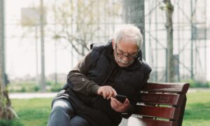 A retiree scrolls on his mobile phone while sitting on a park bench