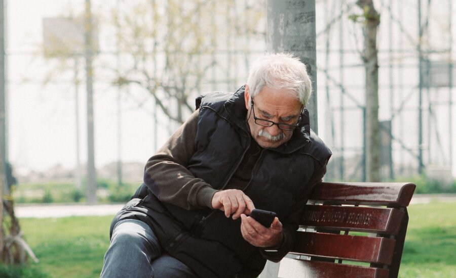 A retiree scrolls on his mobile phone while sitting on a park bench