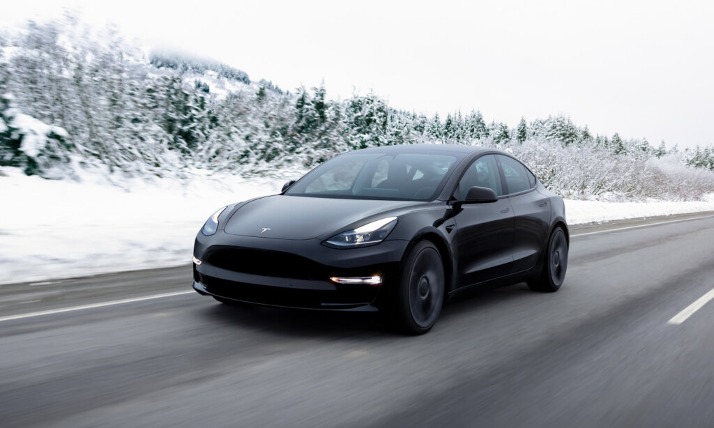A black Tesla Model 3 drives on a highway
