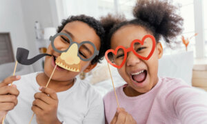 A young brother and sister laugh as they play with funny masks