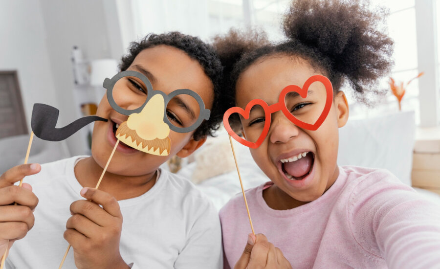 A young brother and sister laugh as they play with funny masks