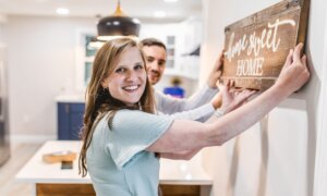 A young couple hangs a "home, sweet home" sign in their new condo