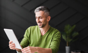 A smiling man in his forties looks at his financial info on a tablet