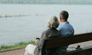 A couple sits on a bench overlooking a waterfront