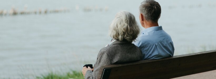A couple sits on a bench overlooking a waterfront