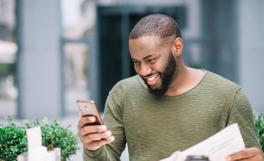 A smiling man checks stock market performance on his phone