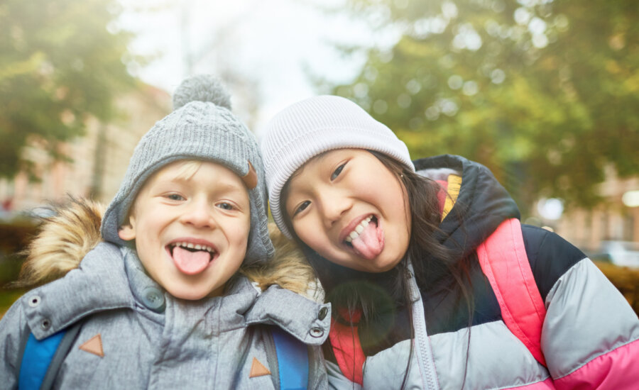 Two young kids in winter clothes smile and stick out their tongues