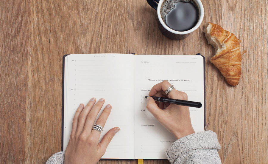 A person writes their financial goals and new years resolutions in a notebook.