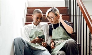 Two young women in work aprons look at a smartphone