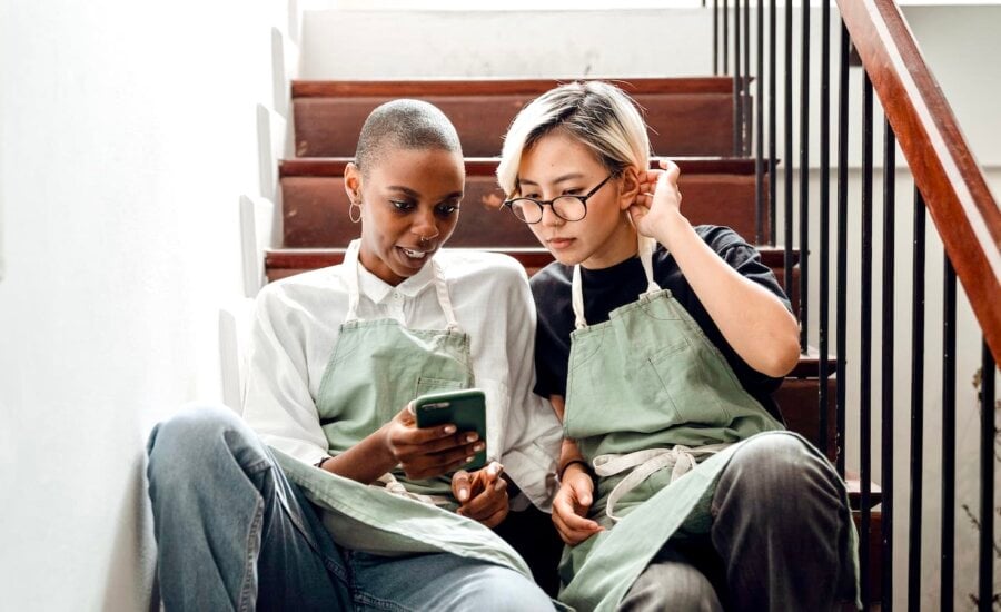 Two young women in work aprons look at a smartphone