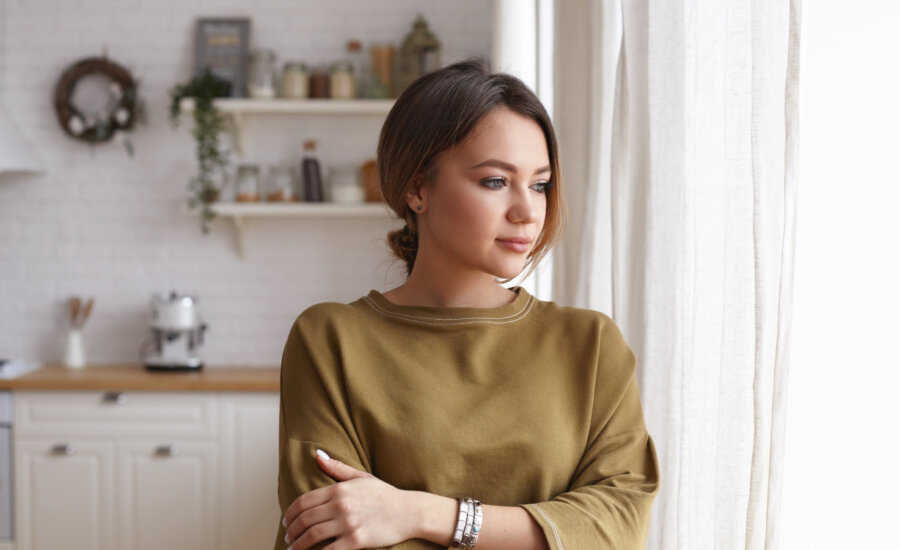 A worried young woman looks out her kitchen window