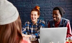 Three young adults chat in a cafe with a laptop on the table