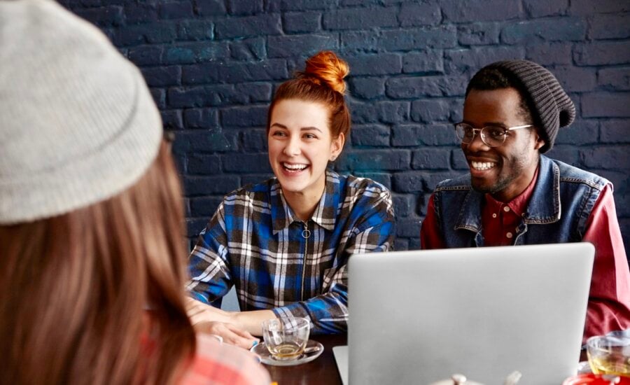 Three young adults chat in a cafe with a laptop on the table