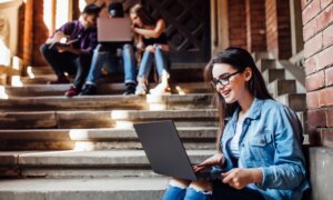 A university student sits with her laptop on her knees