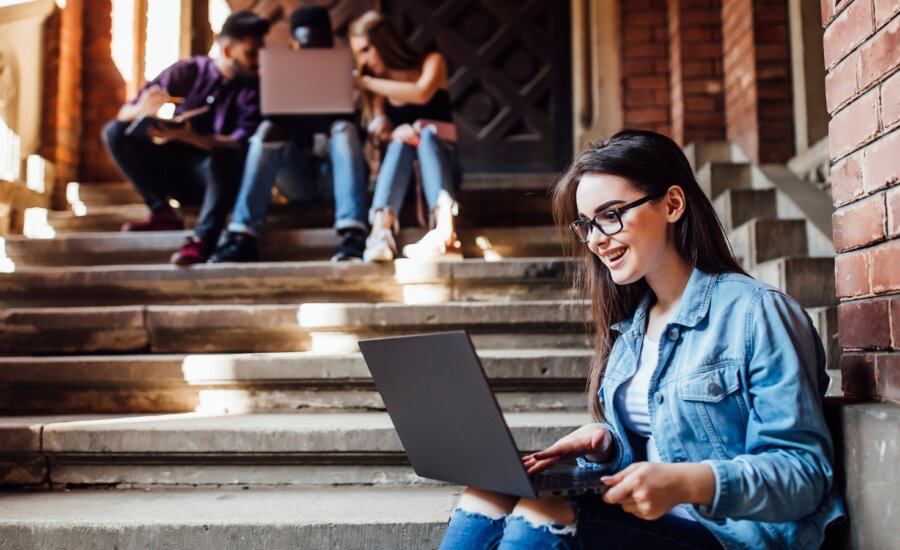 A university student sits with her laptop on her knees