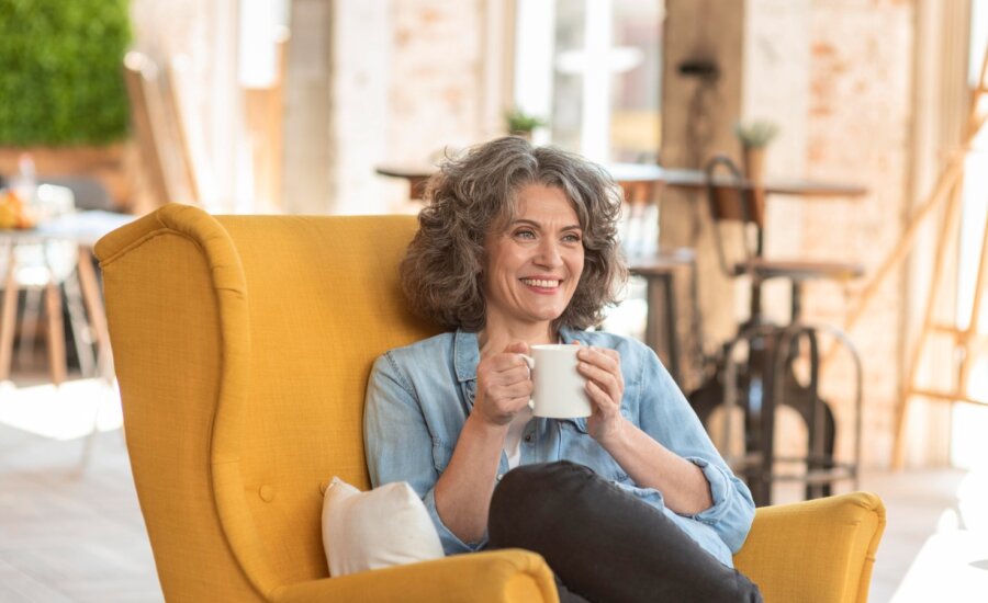 A woman who is nearing retirement sits comfortable in a chair enjoy a coffee