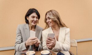 Two women at a cafe smile at GIC rates on their phones