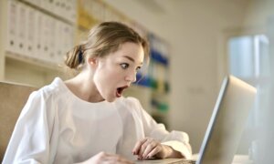 A young woman looks shocked by rising crypto prices on her computer