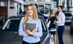 A young car saleswoman standing in front of a car and two customers