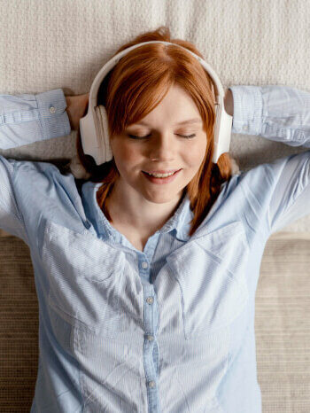 A young woman lies in bed listening to an audiobook on headphones