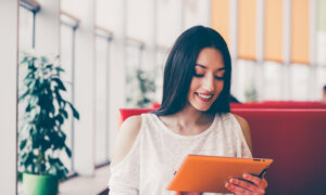 A smiling young woman checks her investments on a tablet